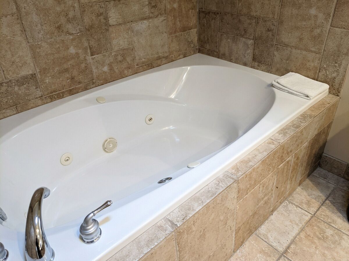 A white bathtub with two faucets and a drain, set against beige tiled walls.