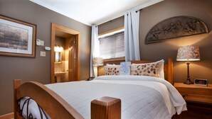 A hotel room with a large bed, wooden headboard, a nightstand with a lamp, a wall clock, and a framed picture.