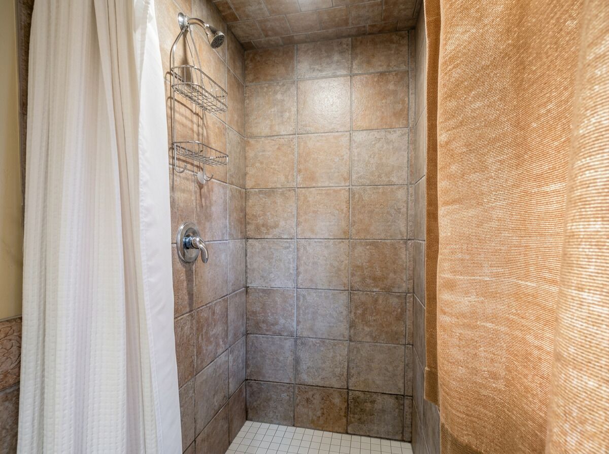 A shower area with tiled walls, a showerhead, and a metal rack.