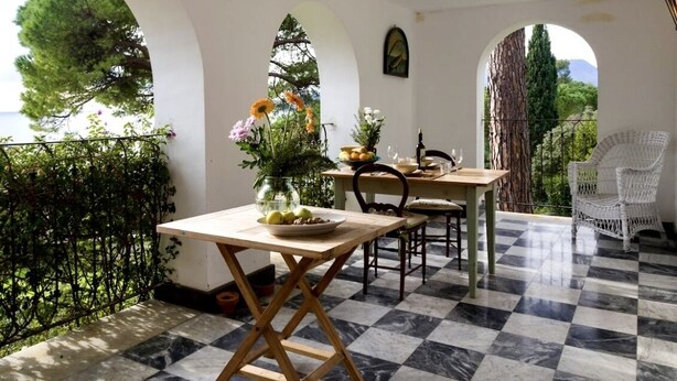 A terrace with a checkered floor, a table with a vase of flowers, and a view of trees and mountains. - Incredible villa facing Portofino (Zoagli)