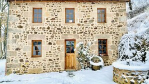Ein Steinhaus mit Holztür, zahlreichen Fenstern und einem mit Schnee bedeckten Dach.