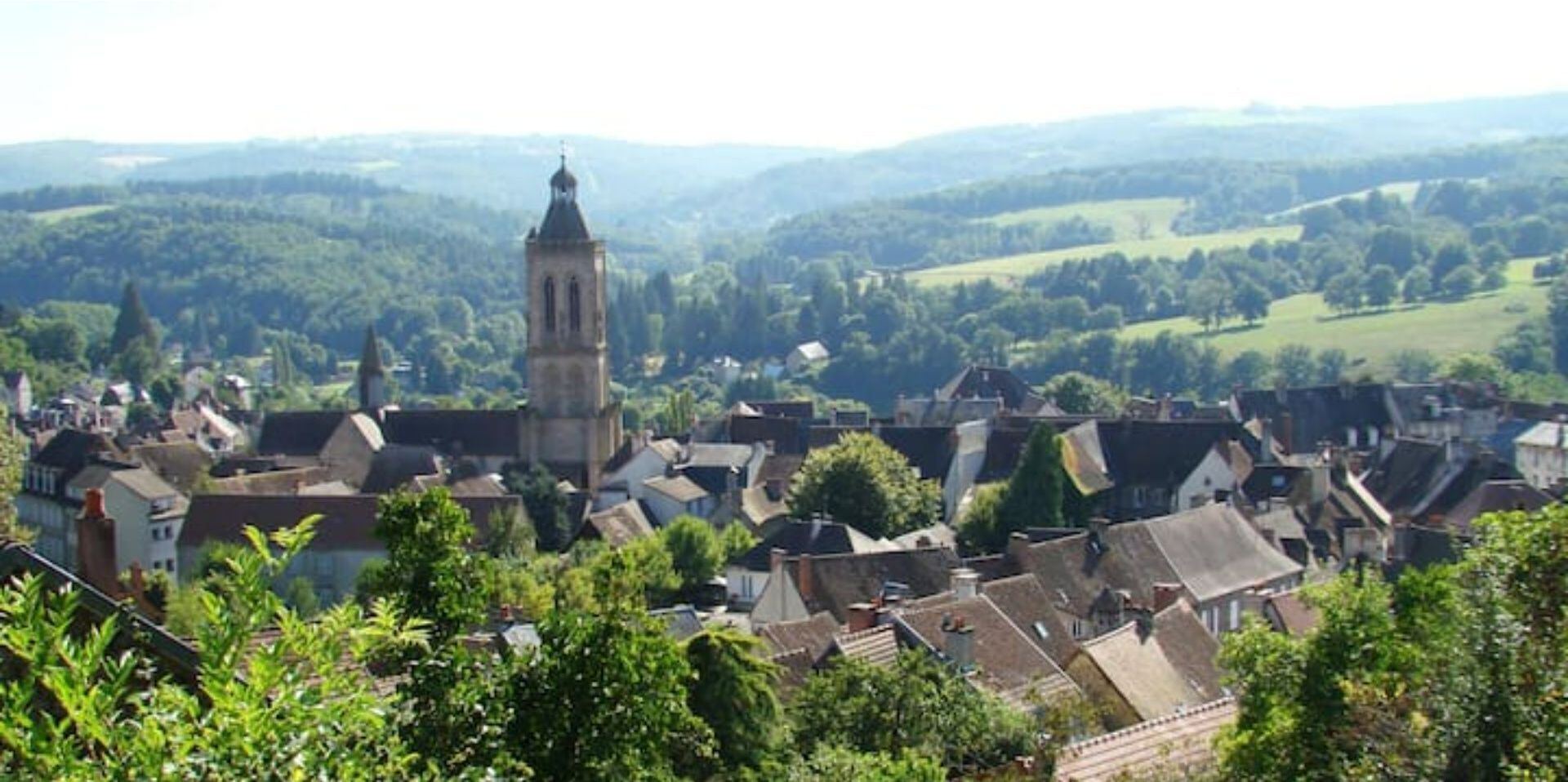 A town with a prominent clock tower, surrounded by traditional buildings and lush greenery.