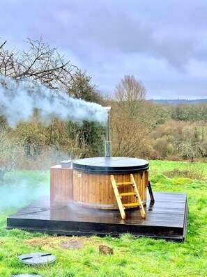 Un bain à remous en bois, équipé d’une échelle, entouré d’une zone herbeuse et d’arbres.