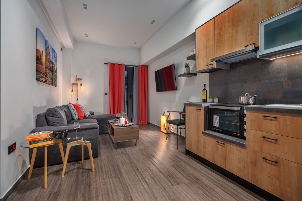 A compact living space with a kitchenette, a sofa, a coffee table, and a TV mounted on the wall.