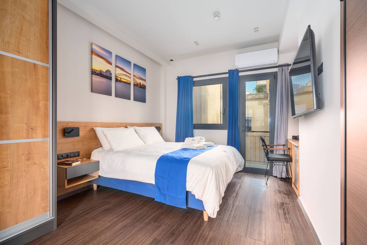 A modern hotel room with a large bed, a flat-screen TV, and a balcony with curtains.