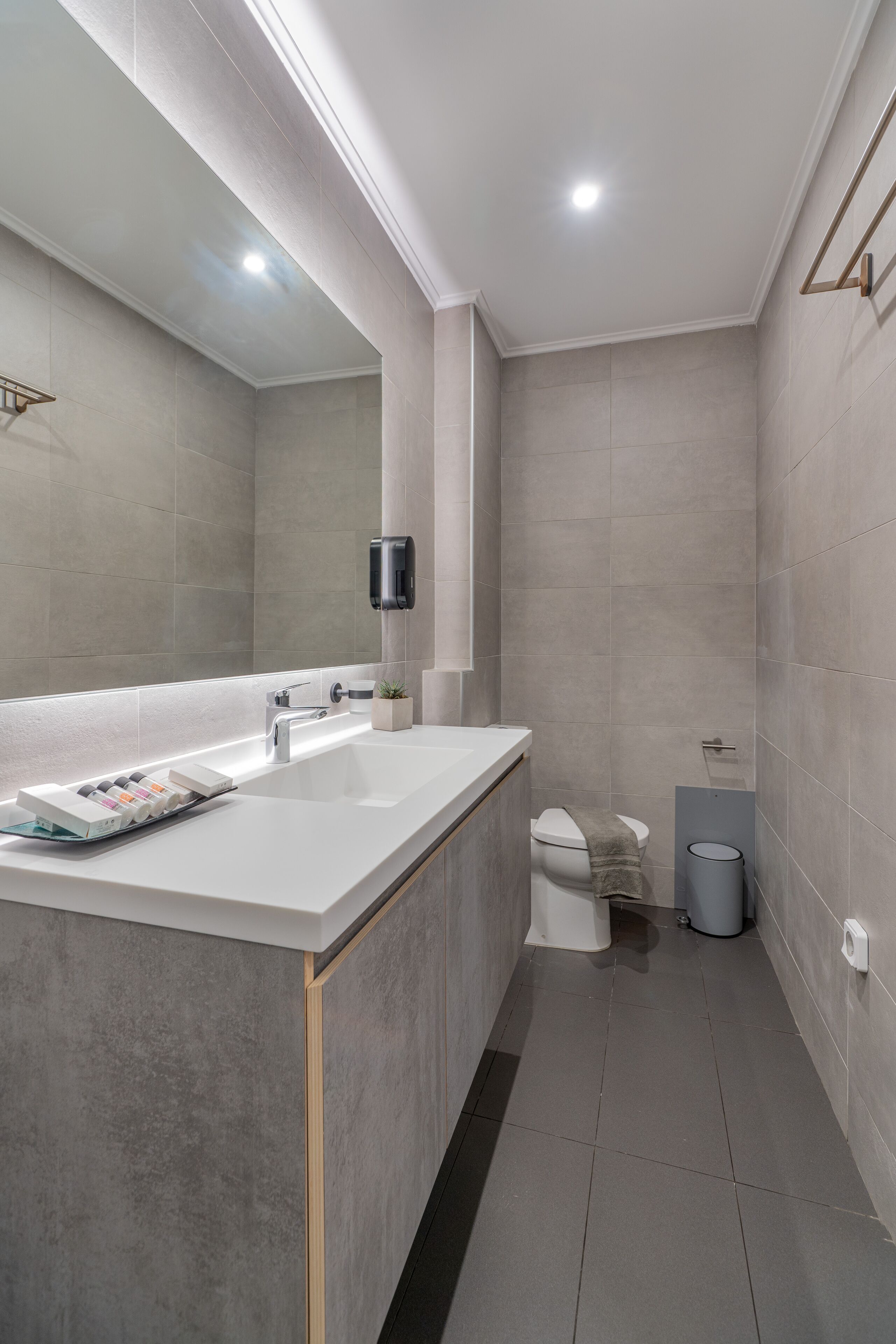 A modern bathroom with a large mirror, a white sink, and a toilet.