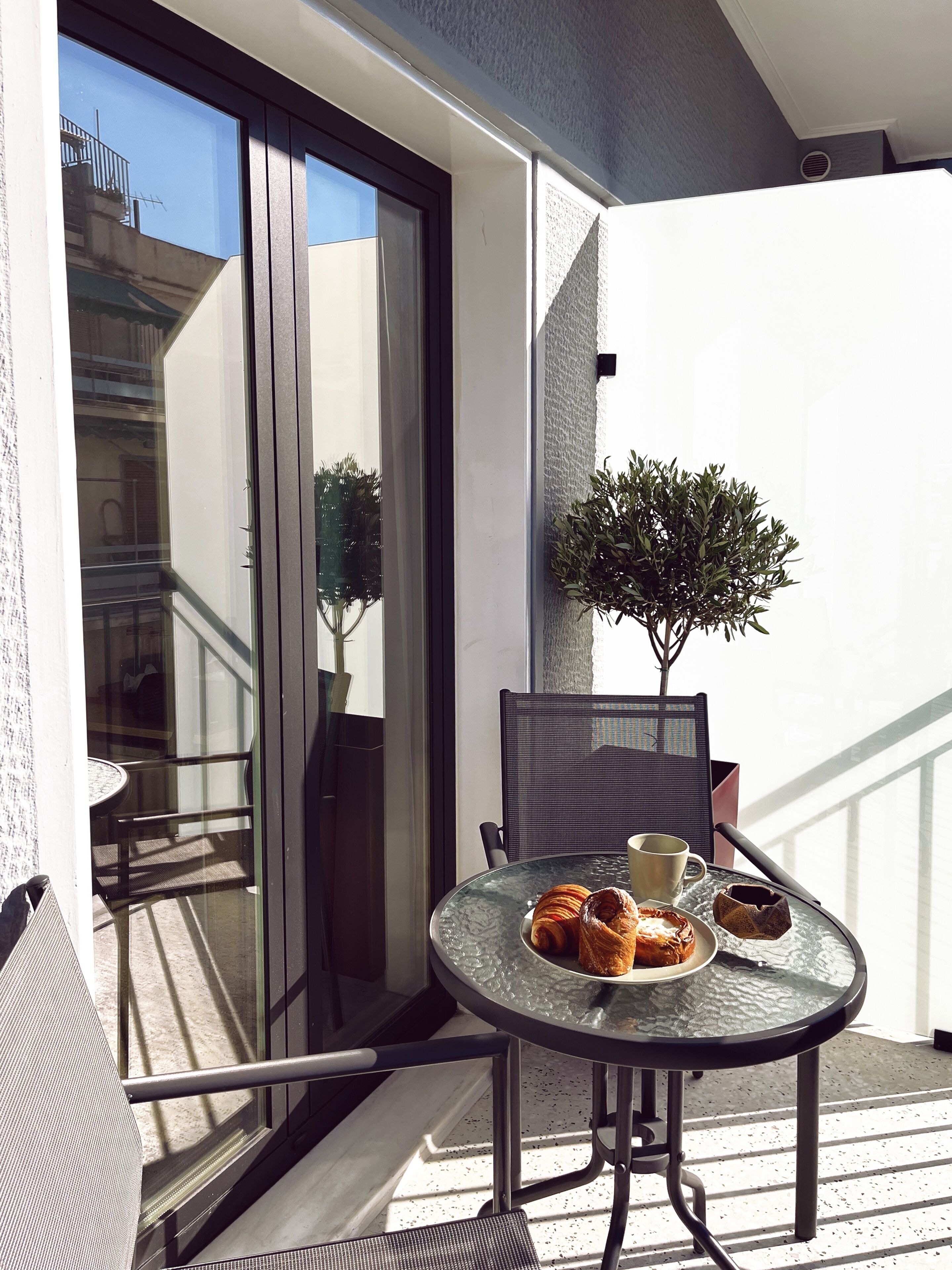 A balcony with a glass table, a chair, a potted plant, and a croissant on the table.