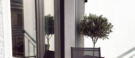 A balcony with a glass table, a chair, a potted plant, and a croissant on the table.