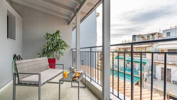 A balcony with a sofa, a table with a tray of food and a drink, and a potted plant.