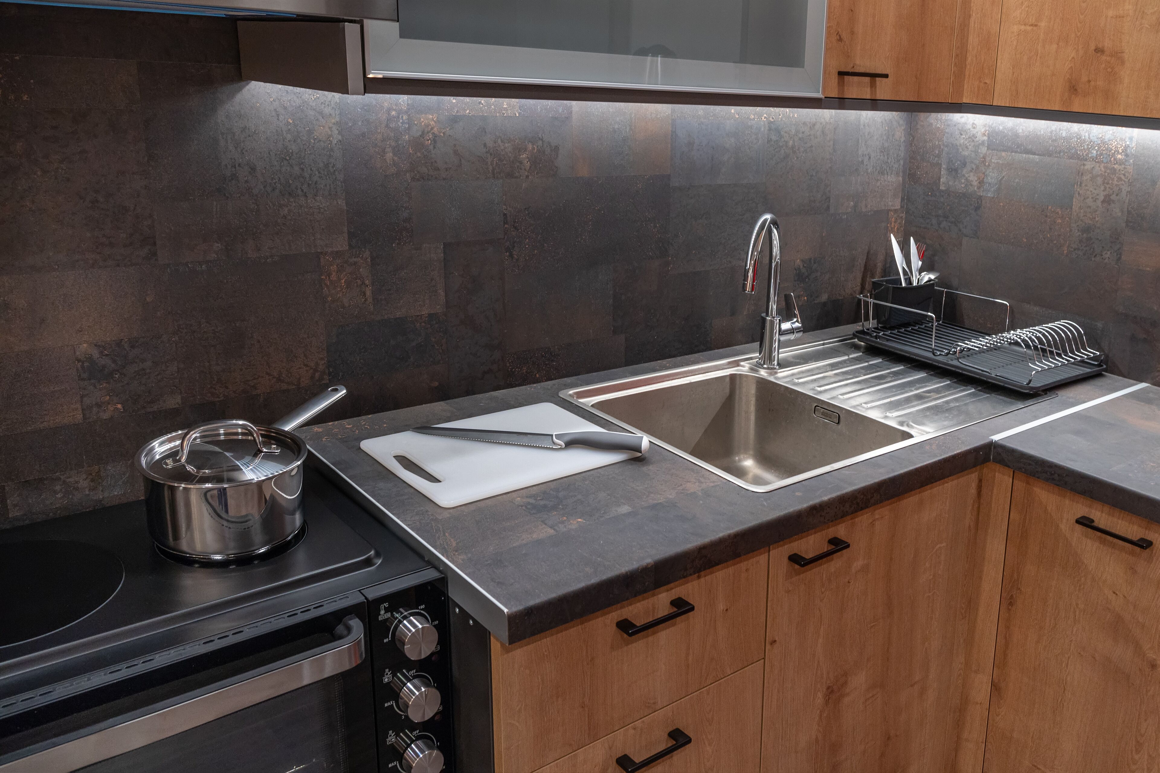 A modern kitchen with a stainless steel sink, a pot on the stove, and a dish rack.