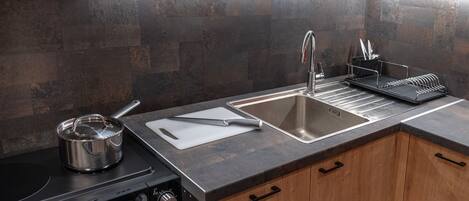 A modern kitchen with a stainless steel sink, a pot on the stove, and a dish rack.