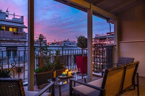 Un balcon avec des fauteuils en osier, une table avec des bougies et une vue sur le paysage urbain au coucher du soleil.