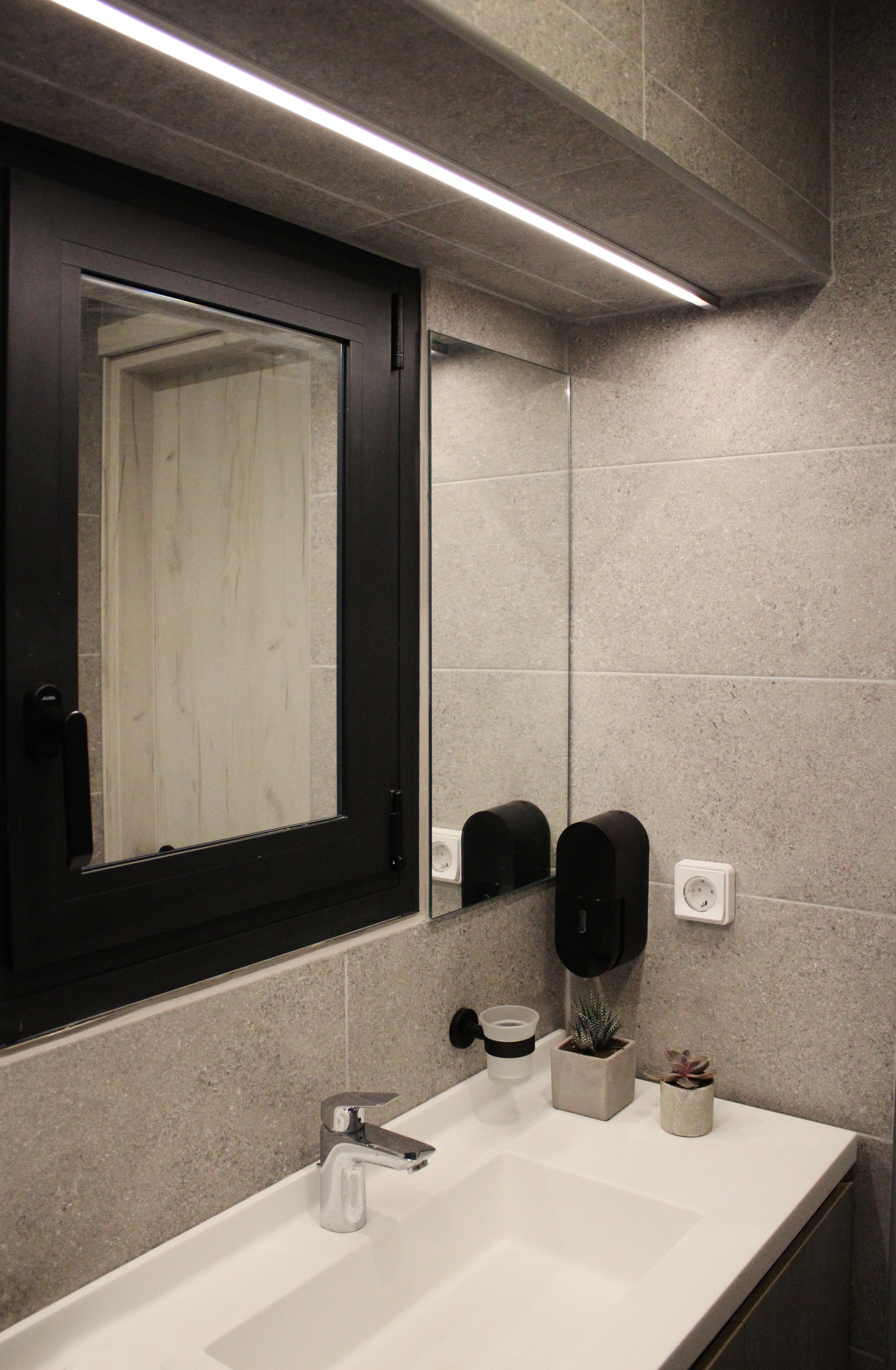 A modern bathroom with a white sink, a mirror with a black frame, and two wall-mounted soap dispensers.