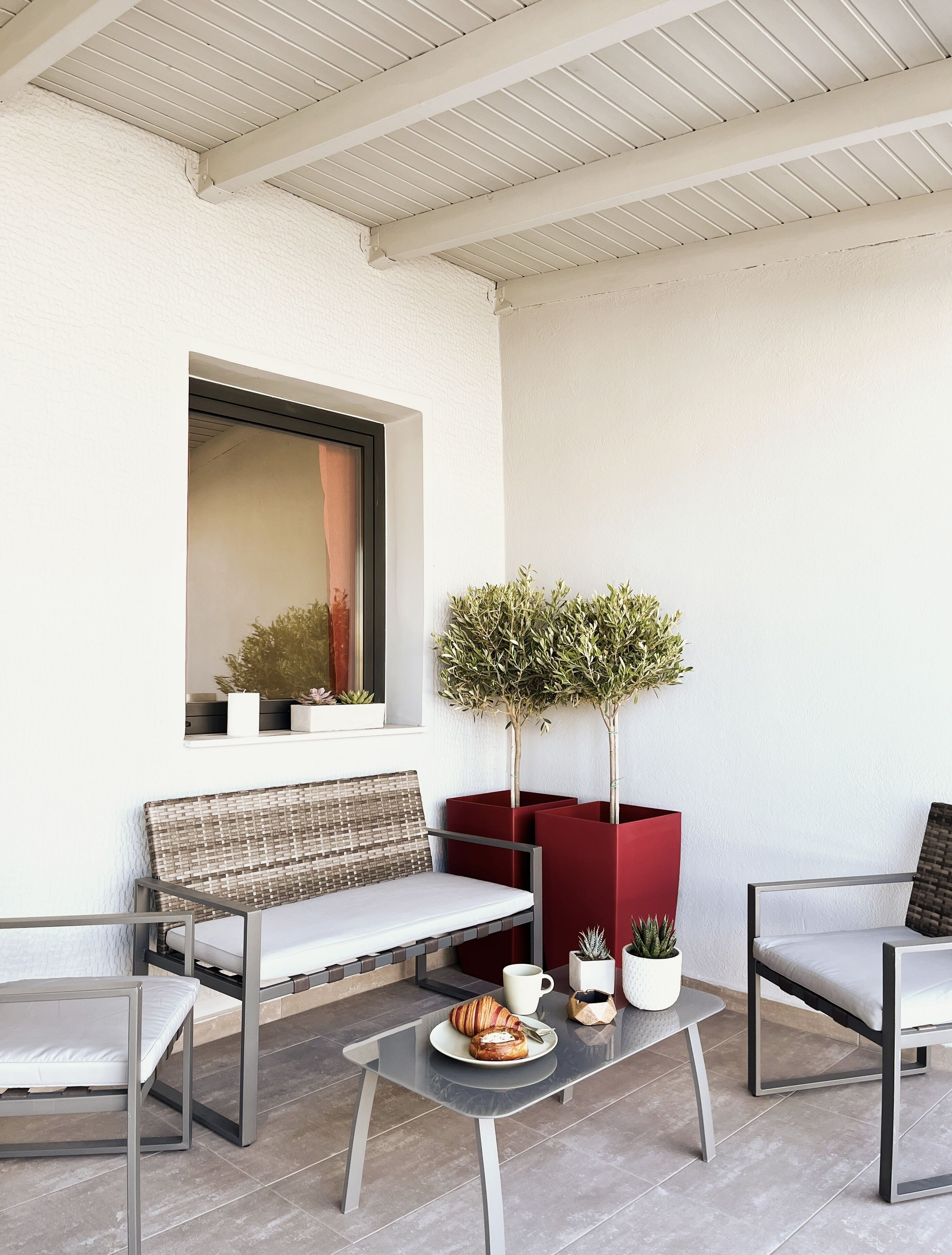 A modern outdoor seating area with a bench, two chairs, a table with a croissant, and potted plants.