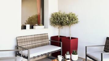 A modern outdoor seating area with a bench, two chairs, a table with a croissant, and potted plants.