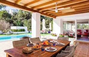 Un espacio exterior para comer con piscina, mobiliario de mimbre y vistas a un edificio residencial.
