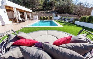 A poolside area with a curved seating arrangement, a pool, and a stone wall in the background. - CAN PARRAS: Family home with a pool and barbecue, 3-minute walk from the beach (Sant Josep de sa Talaia)