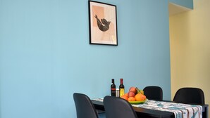 A dining area with a blue wall, a framed artwork, a table with a patterned tablecloth, black chairs, and a fruit bowl. - Elounda Holidays Argyro (Schisma Elountas)