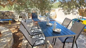 An outdoor dining area with stone flooring, metal chairs, and a blue table set with plates and glasses. - Elounda Holidays Argyro (Schisma Elountas)