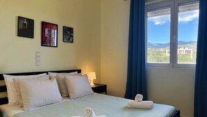 A hotel room with a bed, pillows, a nightstand with a lamp, and framed pictures on the wall. - Elounda Holidays Argyro (Schisma Elountas)