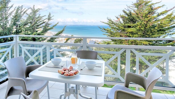 Un balcon avec une table préparée pour le petit-déjeuner, offrant une vue sur la côte.