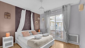 A modern bedroom with a large bed, a bedside table with a lamp, and a view of the city through a large window. - Prat d'Albis - Appt avec terrasse (Toulouse)