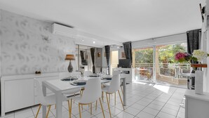A modern kitchen with white cabinetry, a dining area with white chairs, and a balcony with a view of greenery. - Prat d'Albis - Appt avec terrasse (Toulouse)