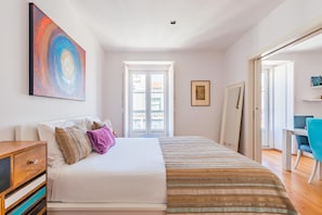 A bedroom with a bed, a desk, a chair, a painting, and a door leading to a balcony. - Lisbon Prime Apartment (Lisbon)