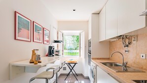 A modern kitchen with white cabinets, a built-in oven, a sink, and a window providing a view of greenery outside. - Lisbon Prime Apartment (Lisbon)