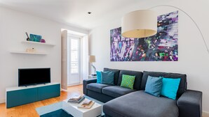 A modern living room with a grey sofa, a flat-screen TV on a teal console, and a colorful abstract painting above the sofa. - Lisbon Prime Apartment (Lisbon)