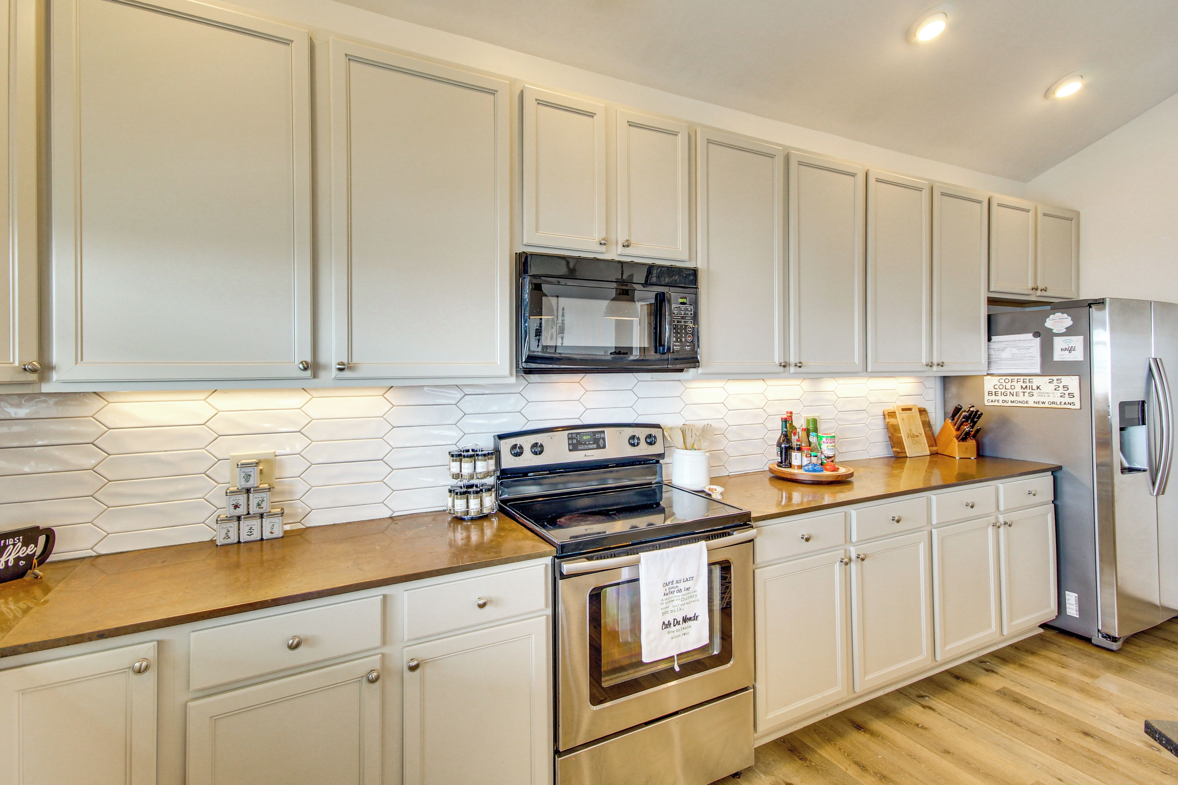 A kitchen with white cabinets, a stainless steel refrigerator, a microwave, and a stove.