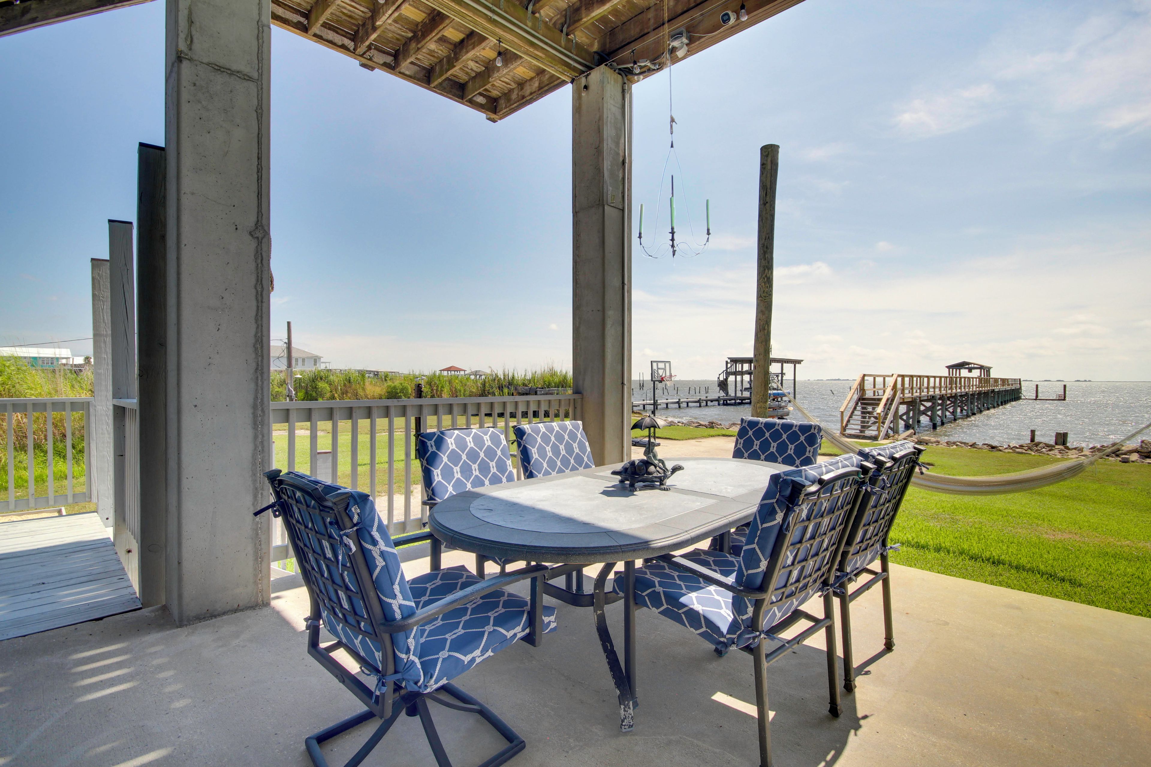 Un patio al aire libre con una mesa y sillas, con vista a un cuerpo de agua y un muelle.