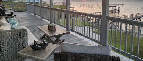 Una terraza techada al aire libre con muebles de mimbre, una mesa con un bol y vistas al atardecer sobre el agua.
