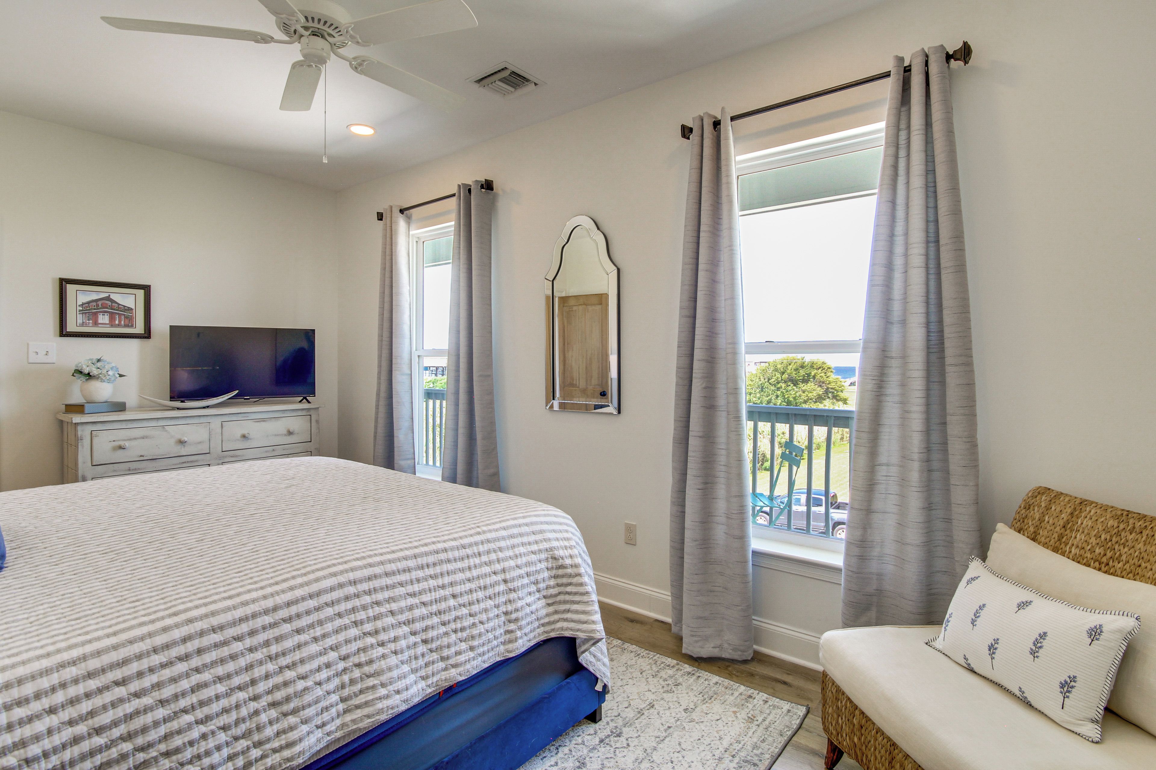 Un dormitorio con cama, cómoda, televisor, ventana con cortinas y balcón.