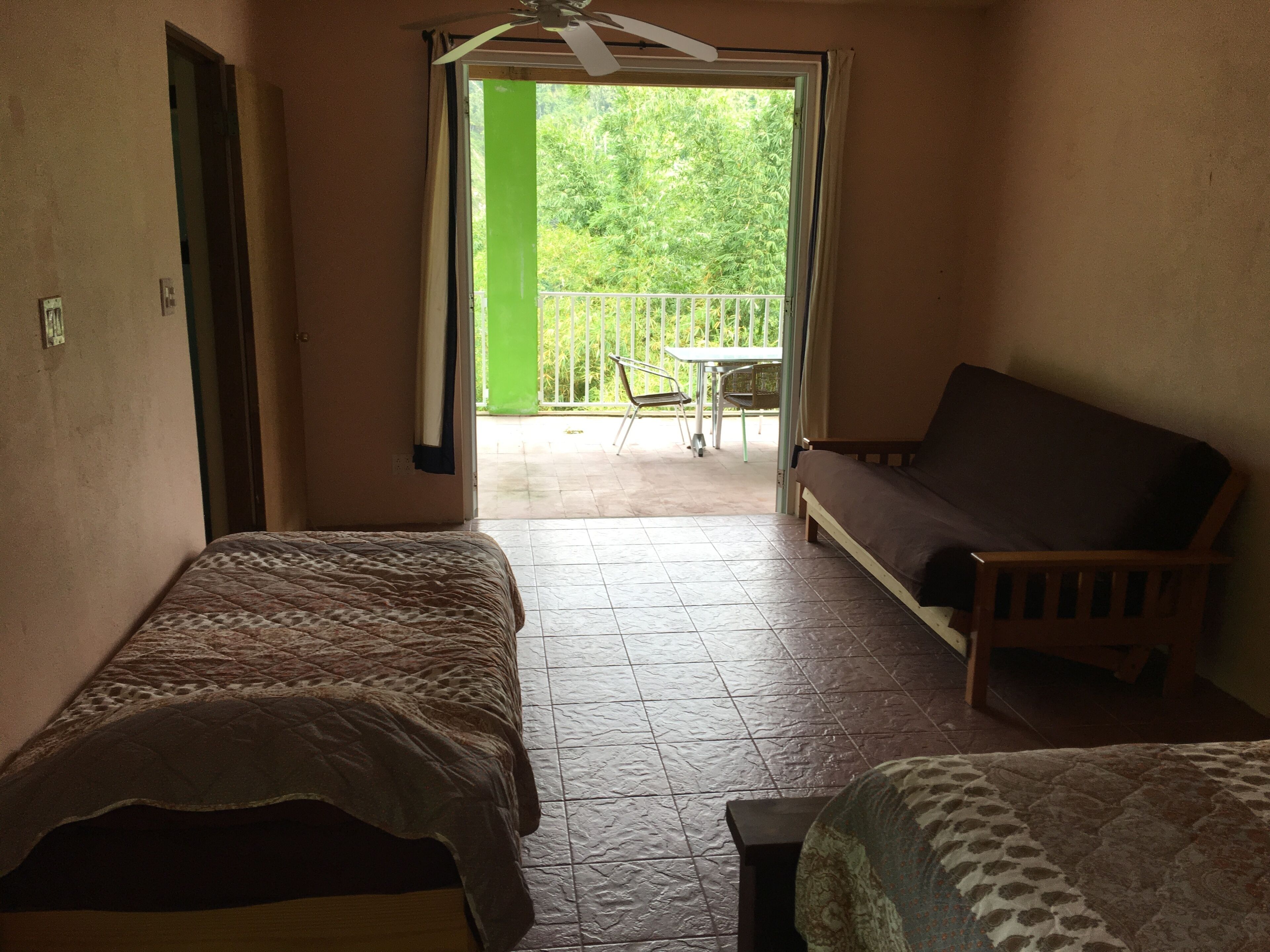Ein Zimmer mit zwei Betten, einem Balkon mit Tisch und Stühlen sowie einem Deckenventilator.