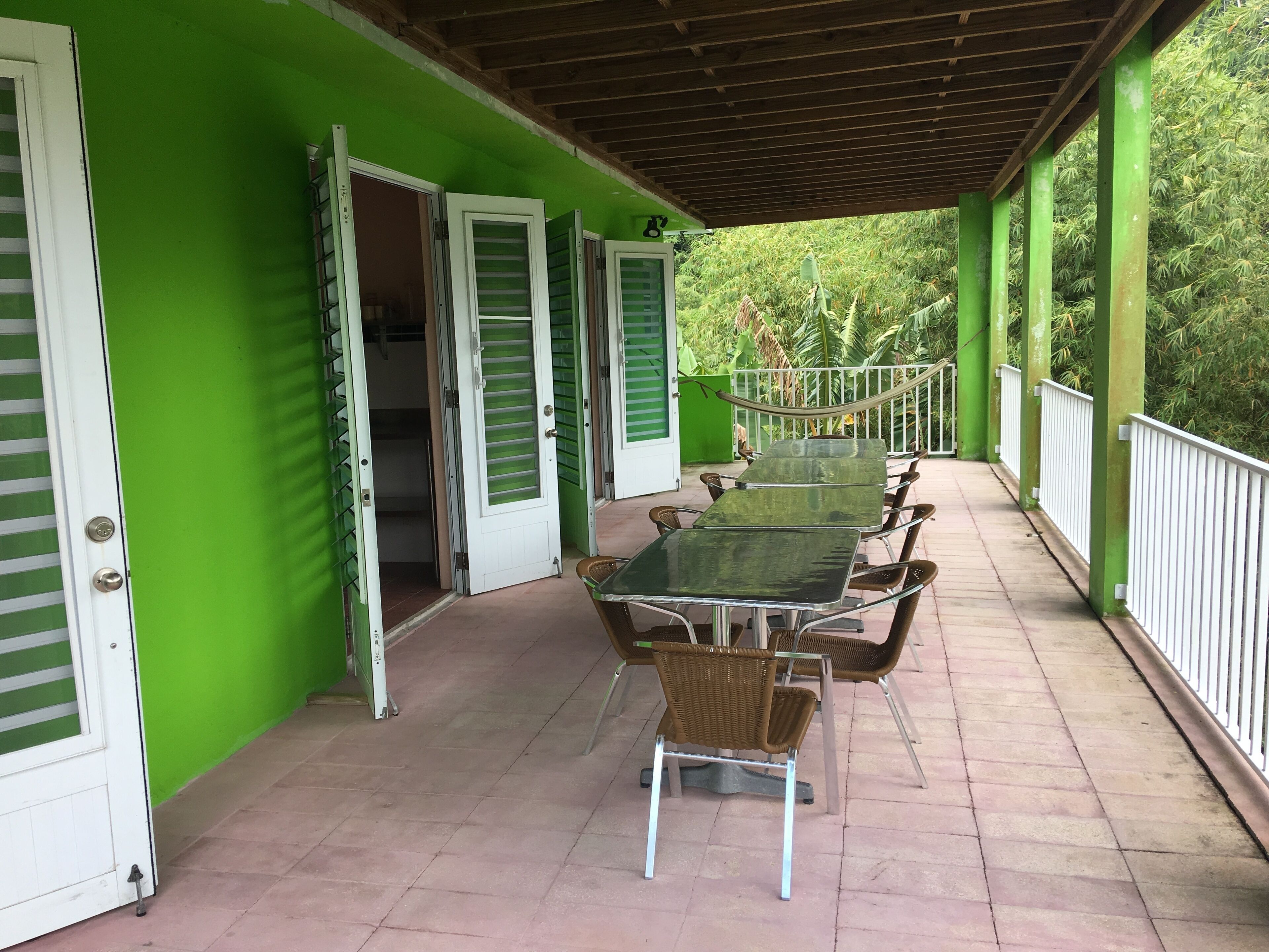 A covered outdoor area with a long table and chairs, green walls, and a white railing.