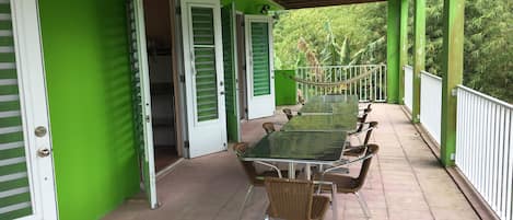 A covered outdoor area with a long table and chairs, green walls, and a white railing.