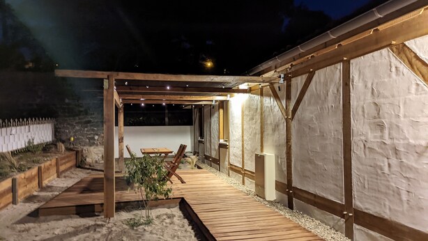 An outdoor wooden deck with a pergola, a seating area, and a stone wall.