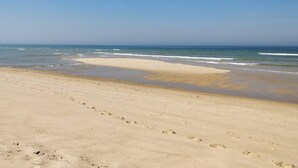 A wide sandy beach with footprints leading to the water, and a clear blue sky above.