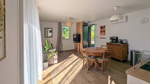 A spacious living area with a wooden dining table, chairs, a TV, and a kitchen area with a coffee machine.