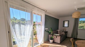 A spacious living area with a sliding glass door leading to a wooden deck, a cozy sofa set, a dining table, and a potted plant.