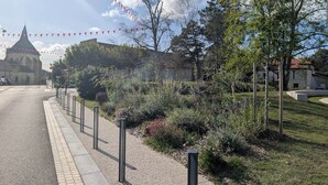 A street with a church, a garden, and a building with a red roof. - Jasmin - Nature & sea with terrace and play area (Lesperon)