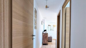 A hallway with wooden flooring and doors, leading to a room with a cabinet and a lamp. - Jasmin - Nature & sea with terrace and play area (Lesperon)