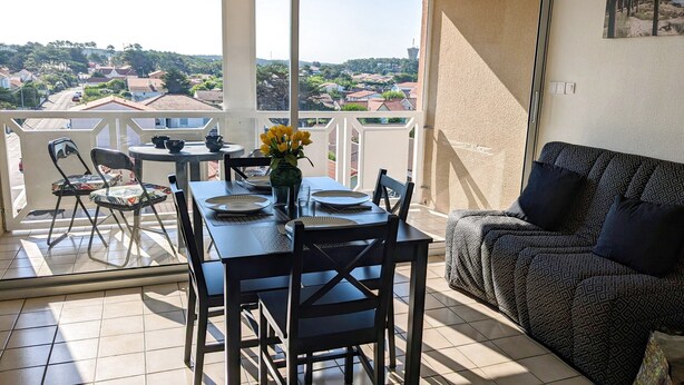 A balcony with a dining table set for four, chairs, a sofa, and a view of a residential area. - Appartement T2 Front de mer (Mimizan)