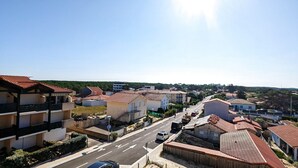 A residential street with houses, a clear sky, and a road with vehicles. - Appartement T2 Front de mer (Mimizan)