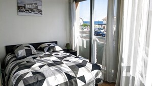 A bedroom with a bed, a nightstand, a lamp, a view of the beach, and a sign on the wall. - Appartement T2 Front de mer (Mimizan)