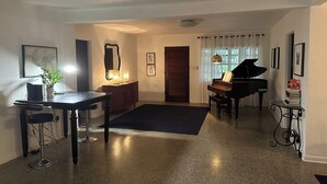 A living room with a piano, a dining table with chairs, a mirror, and a plant. - Quaint Key West Pool Bungalow (Winter Park)