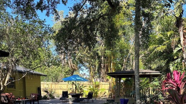 A clear pool with a stone edge, surrounded by a patio with chairs and a small table. - Quaint Key West Pool Bungalow (Winter Park)