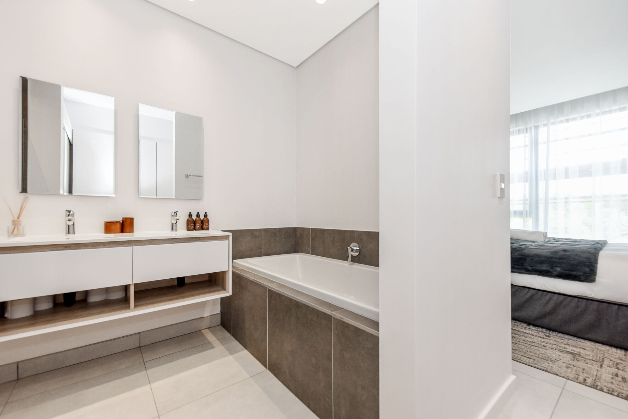 Un baño moderno con una bañera grande, un tocador blanco con espejo y un ventanal que proporciona luz natural.