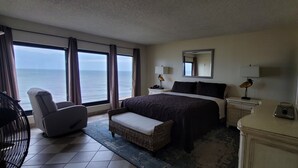 Una habitación de hotel con una cama grande, una silla, una mesita de noche y vista al océano.